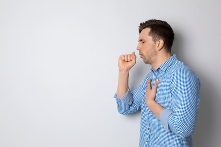 Young man coughing on light backgroundの写真素材