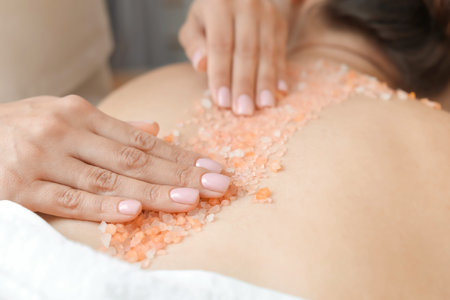 Young woman having body scrubbing procedure with sea salt in spa salon, closeupの写真素材