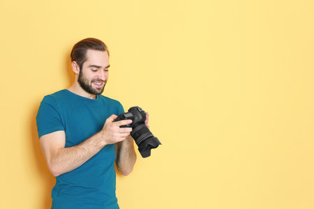 Young photographer with professional camera on color background