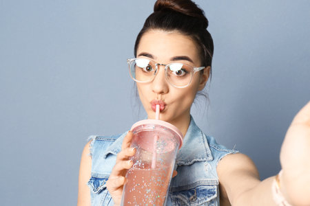 Young beautiful woman taking selfie against gray background