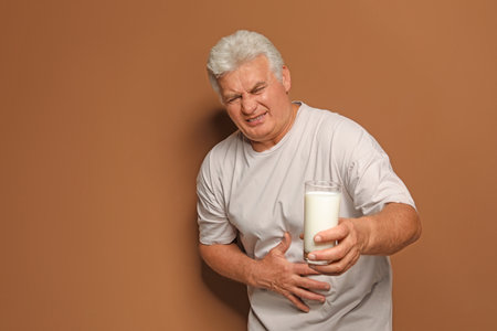 Mature man with dairy allergy holding glass of milk on color backgroundの写真素材