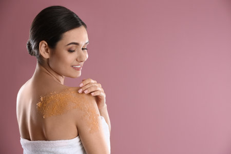 Young woman applying natural scrub on her shoulder against color backgroundの写真素材