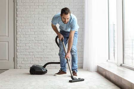 Young man cleaning carpet with vacuum at homeの写真素材