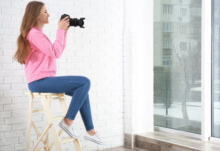 Female photographer with camera sitting on chair indoorsの写真素材