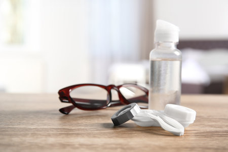 Contact lens case, tweezers, bottle of solution and glasses on tableの写真素材