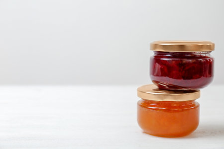 Two jars with tasty sweet jam on white wooden table