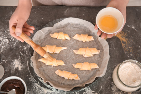 Woman spreading egg yolk on croissants, top view