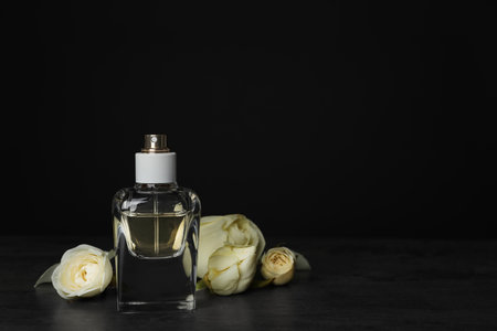 Perfume bottle and flowers on table against black backgroundの写真素材