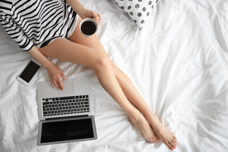 Female blogger with laptop and cup of coffee on bed, top viewの写真素材