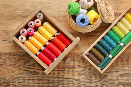 Containers with set of color sewing threads on wooden background