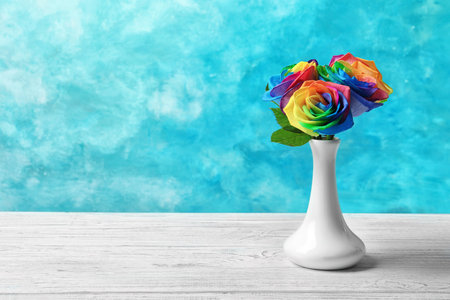 Vase with rainbow rose flowers on table against color backgroundの写真素材