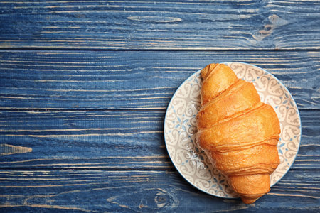 Plate with tasty croissant on wooden background, top viewの写真素材