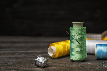 Color sewing threads, needle and thimble on wooden tableの写真素材