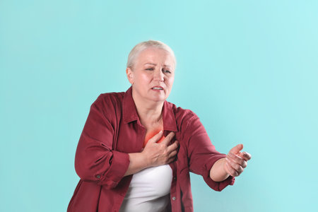 Mature woman having heart attack on color backgroundの写真素材
