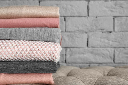 Stack of clean clothes near brick wall indoors