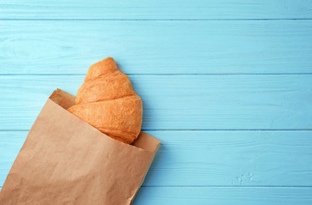 Tasty croissant in paper bag on wooden background, top viewの写真素材