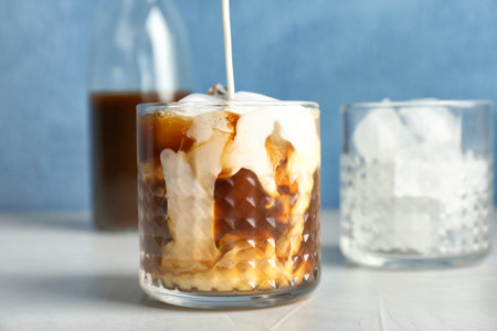 Pouring milk into glass with cold brew coffee on tableの写真素材