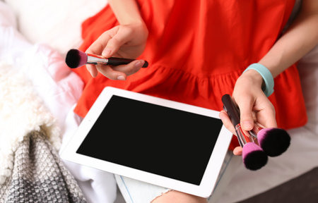 Young woman with makeup brushes using tablet on bed. beauty bloggerの写真素材