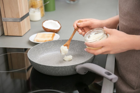 Woman coconut oil on frying putting pan in kitchen, closeupの写真素材