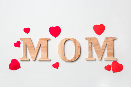 Word "MOM" made of wooden letters and paper hearts on white background. Happy Mother's Dayの写真素材