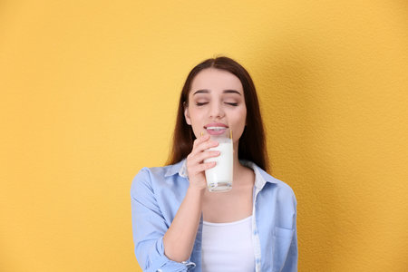 Beautiful young woman drinking milk on color backgroundの写真素材