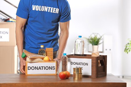 Male volunteer holding donation box with food products indoorsの写真素材
