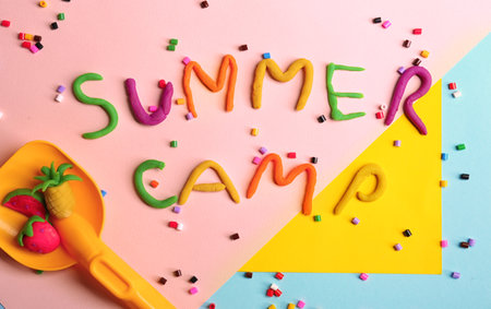 Flat lay composition with words SUMMER CAMP made from modeling clay, beads and plastic shovel on color backgroundの写真素材