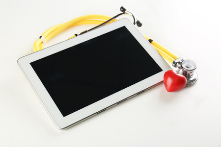 Stethoscope, tablet and small red heart on light background. heart attack conceptの写真素材