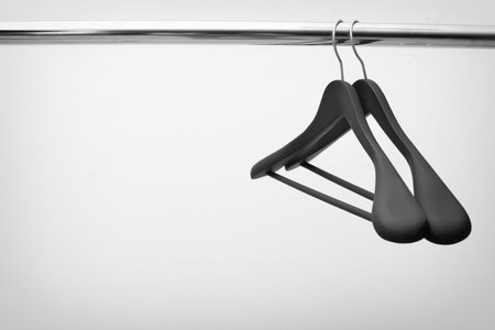 Clothes hangers on metal rail against light backgroundの写真素材
