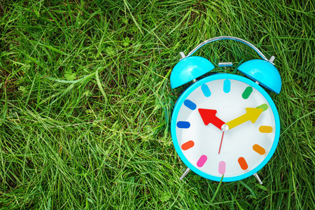 Alarm clock on green grass, outdoors. time change conceptの写真素材