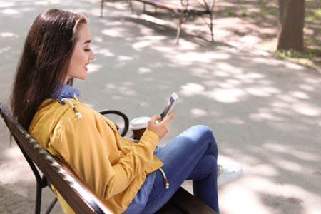Young woman using phone outdoors on sunny dayの写真素材