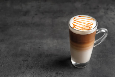 Glass cup with delicious caramel latte on gray background