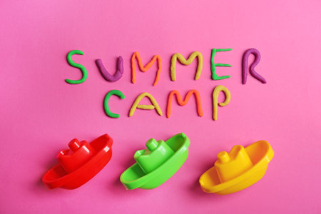 Flat lay composition with words SUMMER CAMP made from modeling clay and plastic boats on color background