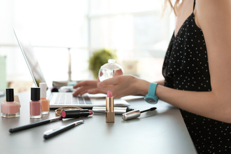 Young woman with makeup products using laptop at table. beauty bloggerの写真素材