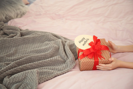 Little child putting gift box for Mother's Day on bedの写真素材