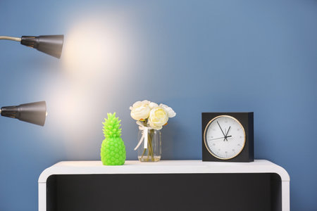 Stylish pineapple candle, flowers and clock on table against color backgroundの写真素材