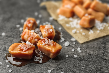 Delicious candies with caramel sauce and salt on gray backgroundの写真素材