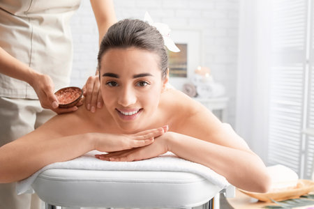 Young woman having body scrubbing procedure with sea salt in spa salonの写真素材