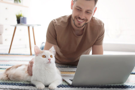 Young man with cute cat and laptop at homeの写真素材