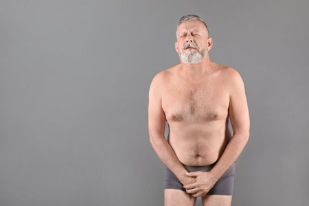 Mature man with urological problems suffering from pain on gray backgroundの写真素材
