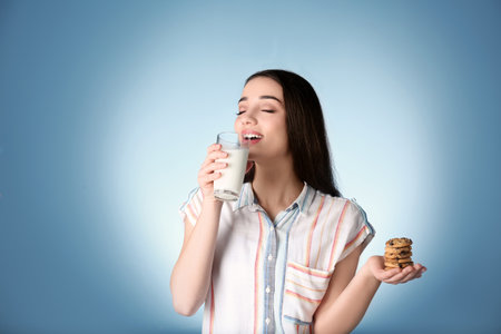 Beautiful young woman drinking milk with cookies on color backgroundの写真素材