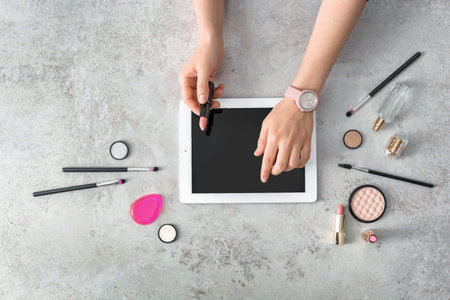 Young woman with makeup products using tablet at table. beauty bloggerの写真素材