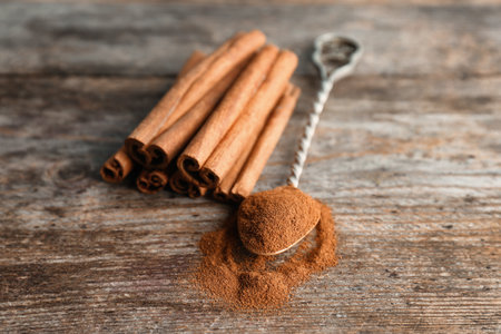 Spoon with aromatic cinnamon powder and sticks on wooden backgroundの写真素材