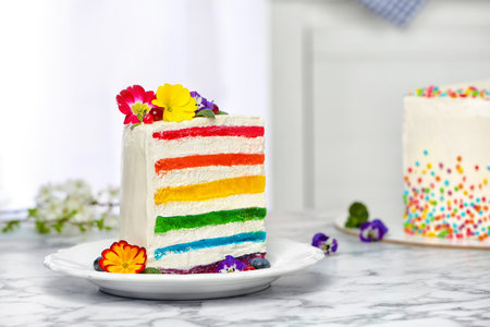 Slice of delicious rainbow cake with flowers on table