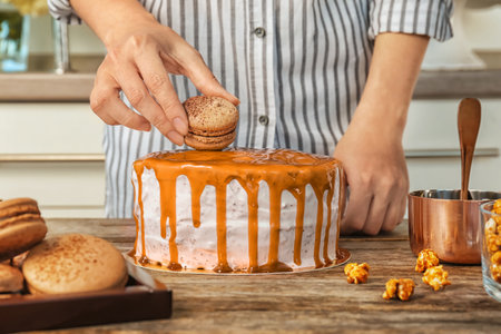 Young woman decorating delicious caramel cake at tableの写真素材