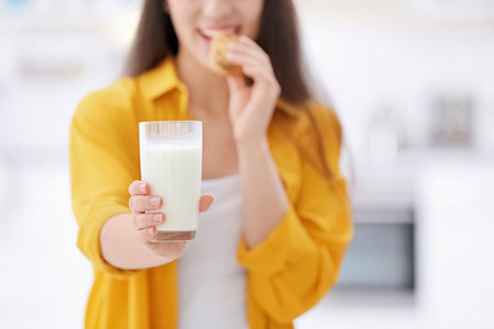 Beautiful young woman drinking milk with cookies at homeの写真素材