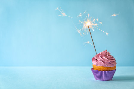 Delicious birthday cupcake with sparkler on color backgroundの写真素材