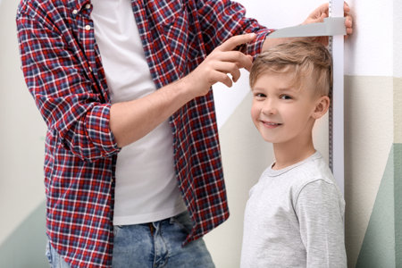 Young man measuring his son's height at homeの写真素材