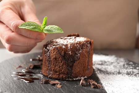 Chef decorating delicious fresh chocolate fondant with mint at table. Lava cake recipeの写真素材