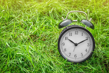 Alarm clock on green grass, outdoors. time change conceptの写真素材